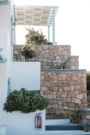 A modern building with a stone facade, a small garden with plants, and a fire extinguisher mounted on the wall. - Asterias Boutique Hotel (Milos)