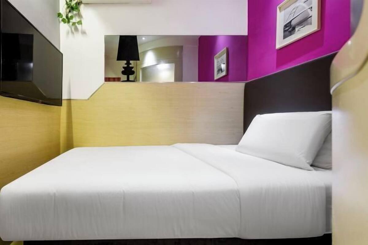 A single bed with white bedding in a room with a wooden headboard and a purple accent wall.
