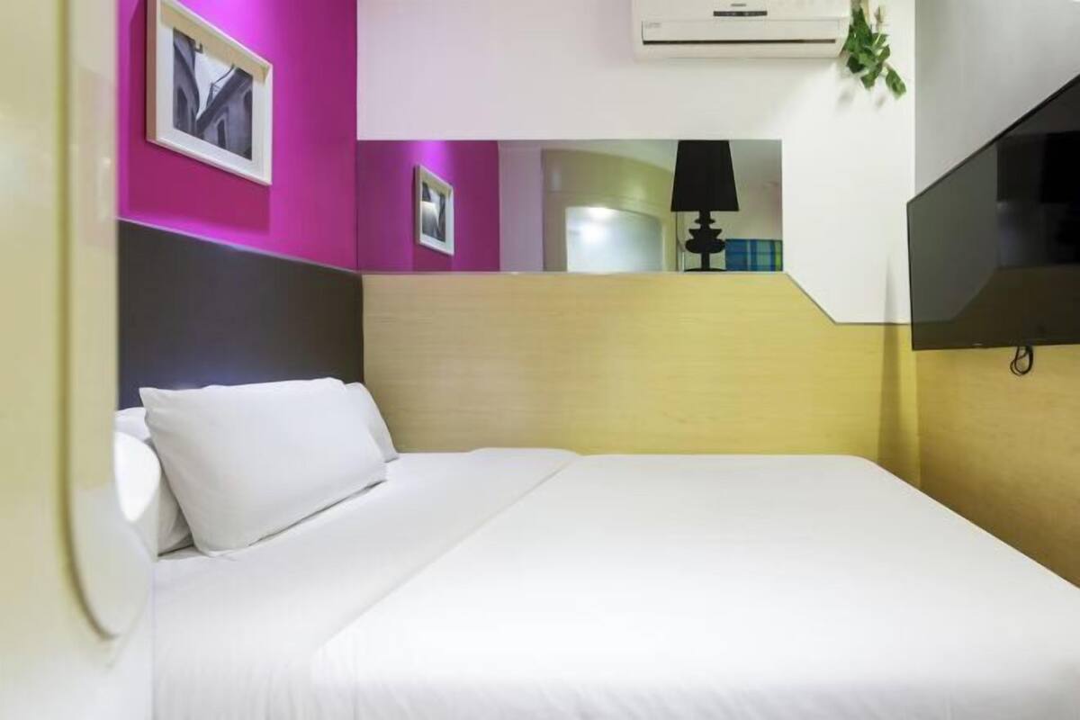 A hotel room with a bed, a wall-mounted air conditioner, and a framed picture.