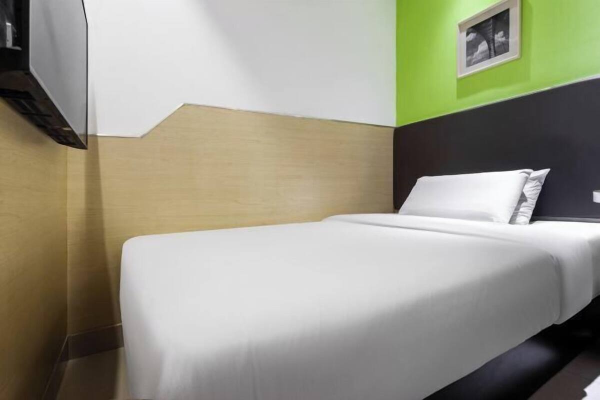 A hotel room with a bed, a flat-screen TV mounted on the wall, and a green accent wall.