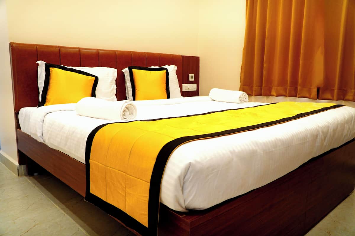 Una habitación de hotel con cabecera de madera, cama con ropa de cama blanca y amarilla, y cortina marrón.