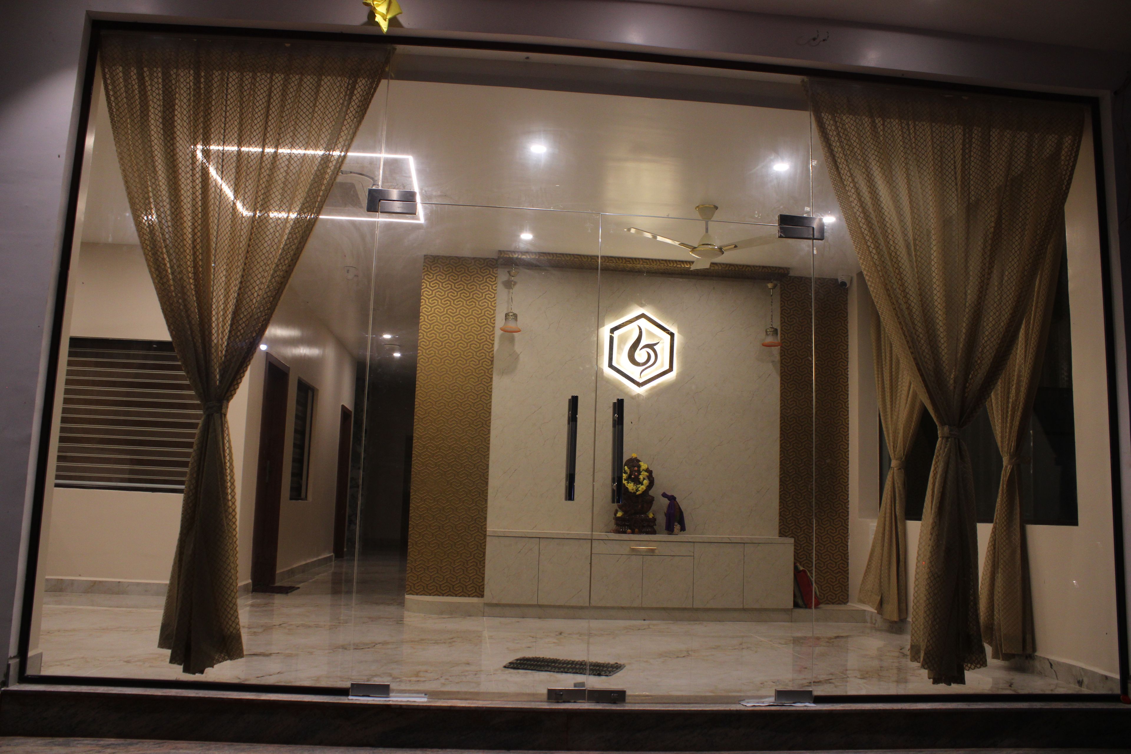 A hotel lobby with a reception desk, a decorative wall with a geometric pattern, and a ceiling fan.