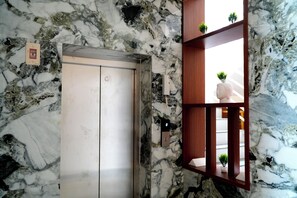 An elevator with a marble wall, a wooden shelf with plants, and a small sign on the wall. - UJ PALLAZZIO - Business Class Luxury Hotel (Tiruvannamalai)
