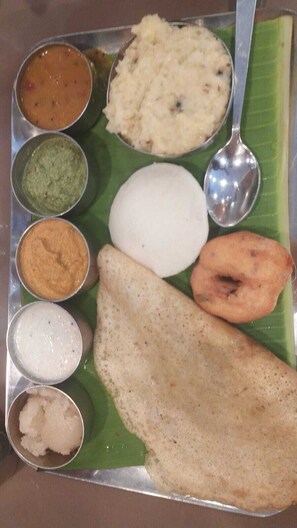 A traditional South Indian meal served on a banana leaf with various accompaniments. - UJ PALLAZZIO - Business Class Luxury Hotel (Tiruvannamalai)