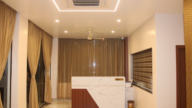 A reception area with a marble counter, a ceiling fan, and a patterned wall. - UJ PALLAZZIO - Business Class Luxury Hotel (Tiruvannamalai)