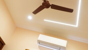 A ceiling fan with a light fixture, an air conditioning unit, and a window with curtains. - UJ PALLAZZIO - Business Class Luxury Hotel (Tiruvannamalai)