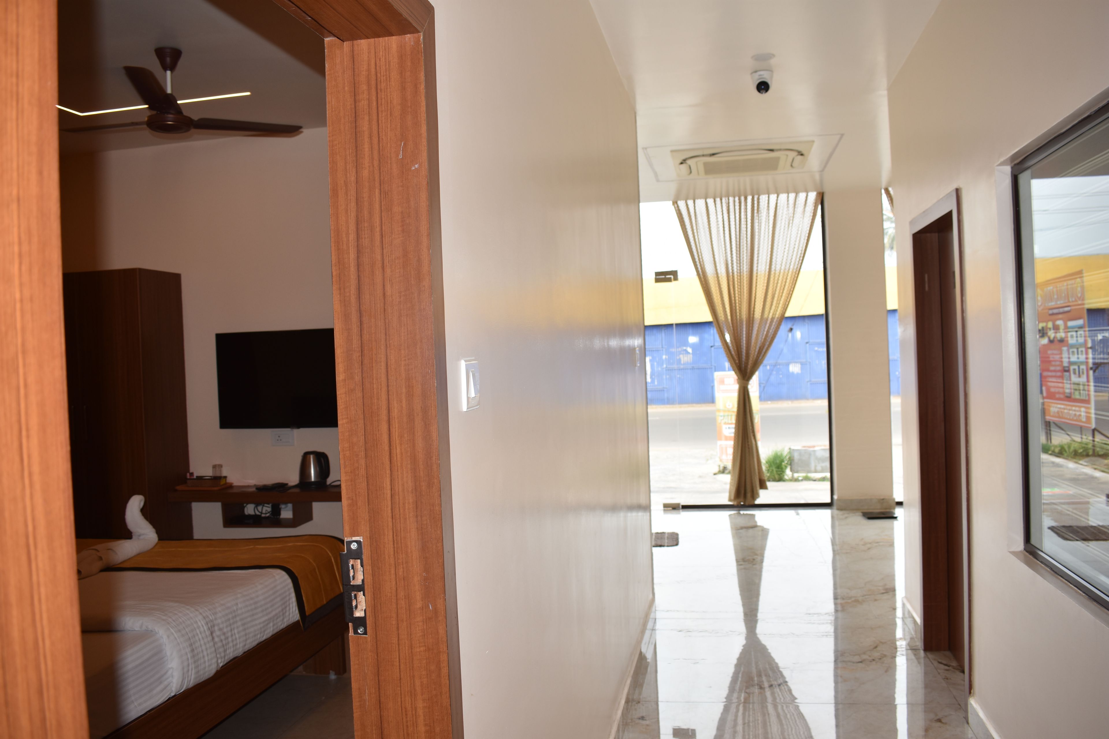 A hotel corridor with a bed, a ceiling fan, a television, and a view of the outside through a window.
