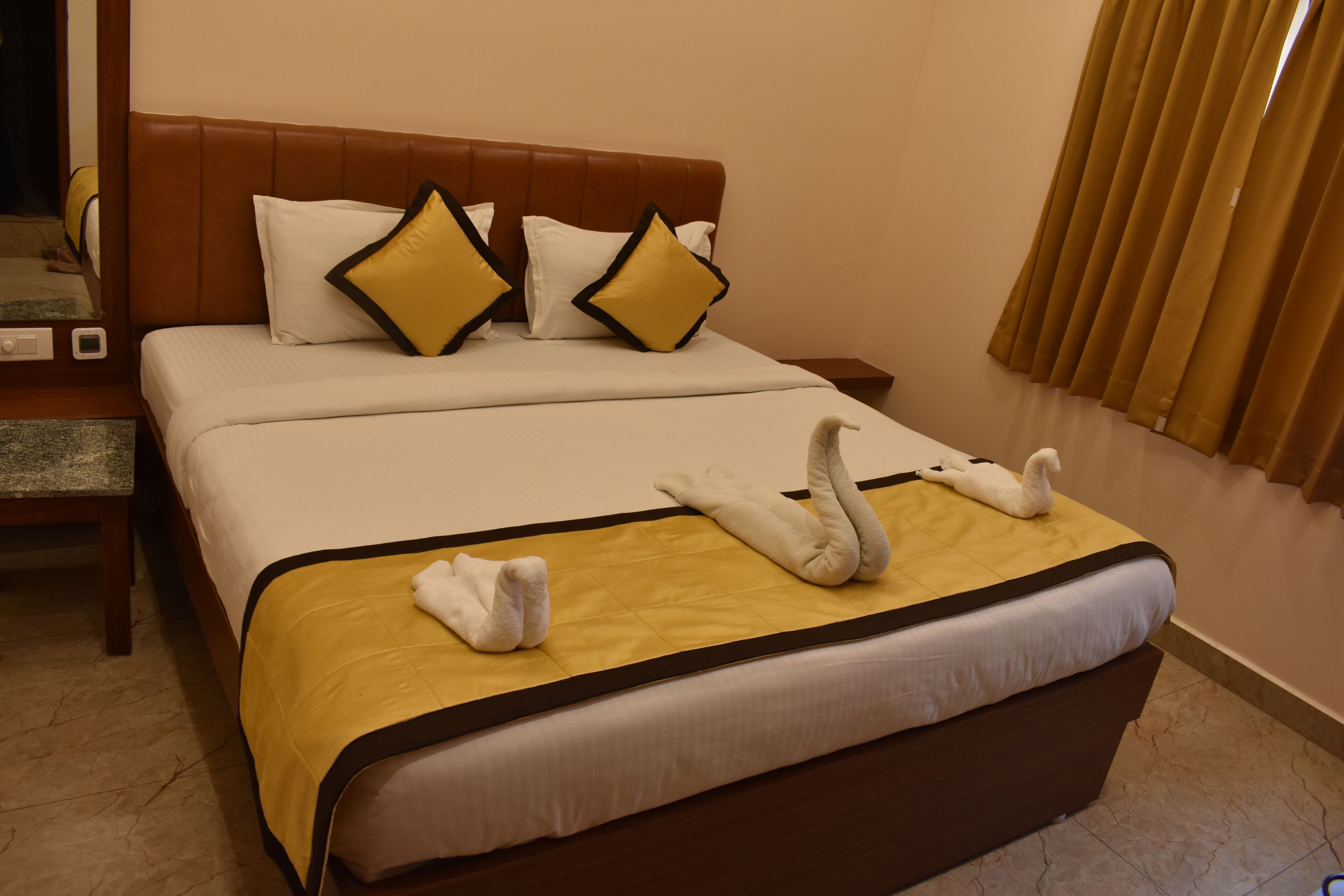 Een hotelkamer met een groot bed, twee kussens, een nachtkastje en een raam met gordijnen.