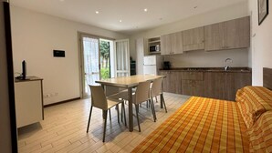 Ein moderner, kompakter Wohnraum mit Essbereich, Küchenzeile und einem Bett mit karierter Bettdecke.