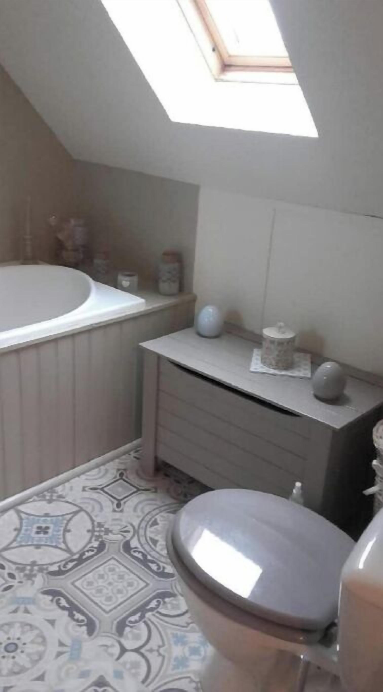 Un baño con tragaluz, bañera, inodoro y tocador con cajones.