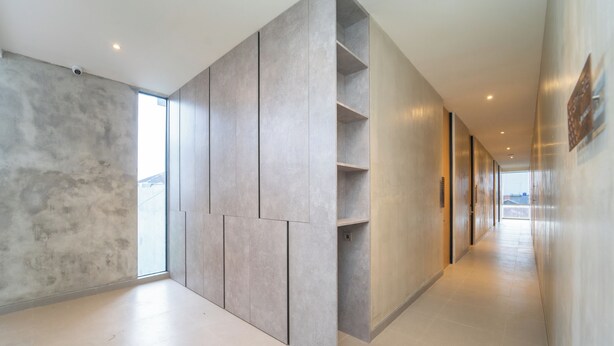 A modern hallway with a minimalist design, featuring a concrete wall with built-in shelving and a glass door leading to a balcony. - Keenan Living Luxe Seturan (Depok)
