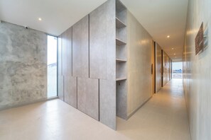A modern hallway with a minimalist design, featuring a concrete wall with built-in shelving and a glass door leading to a balcony. - Keenan Living Luxe Seturan (Depok)