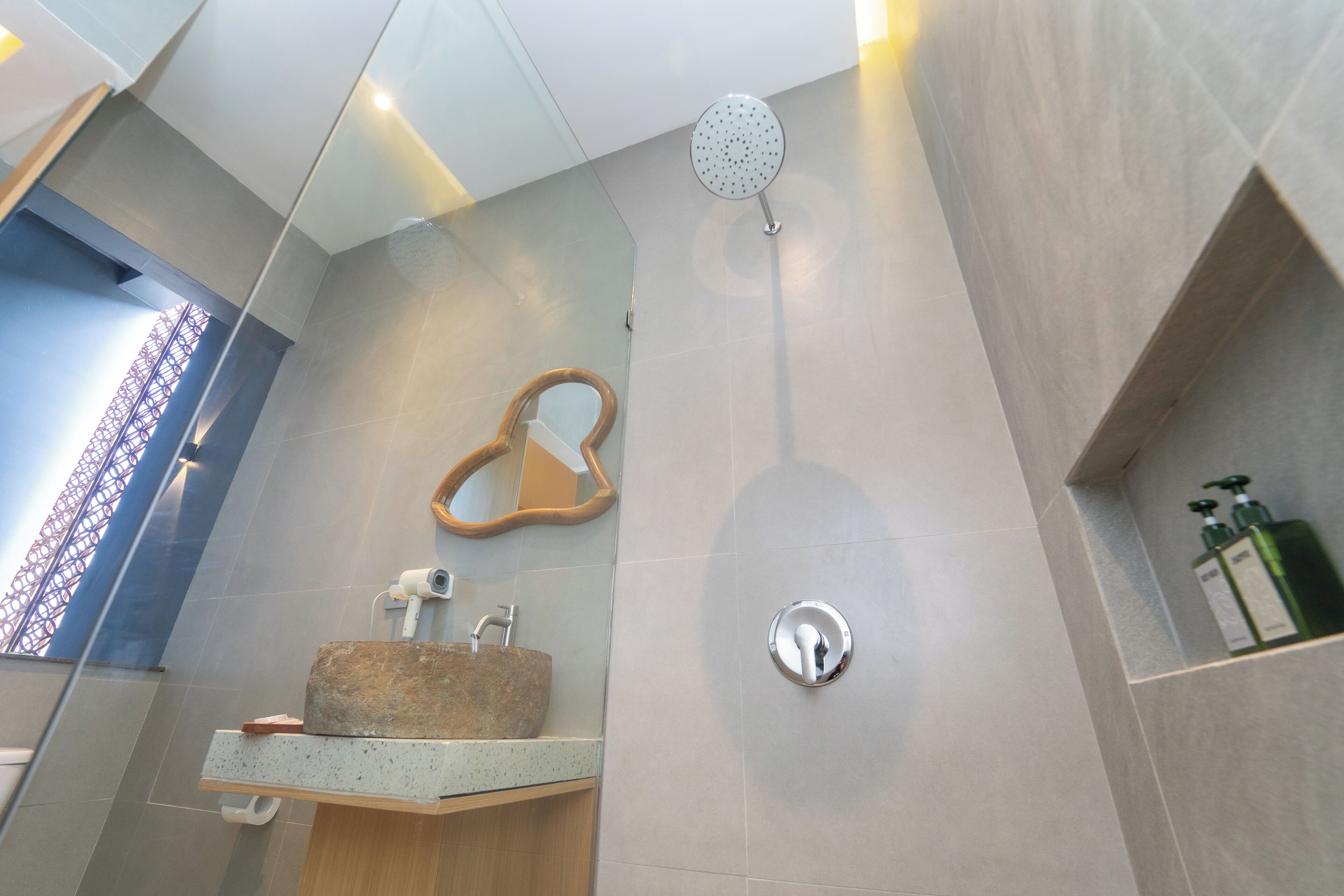 A modern bathroom with a large mirror, a showerhead, and a sink with a stone basin.