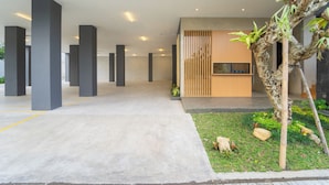A spacious indoor area with concrete flooring, large pillars, a wooden slatted wall, and a small garden with plants and rocks. - Keenan Living Luxe Seturan (Depok)