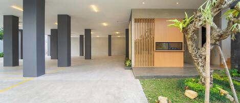 A spacious indoor area with concrete flooring, large pillars, a wooden slatted wall, and a small garden with plants and rocks.