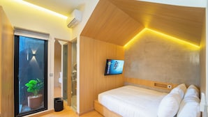 A modern bedroom with a wooden ceiling, a large bed with white bedding, a mounted TV, and a potted plant by the window. - Keenan Living Luxe Seturan (Depok)