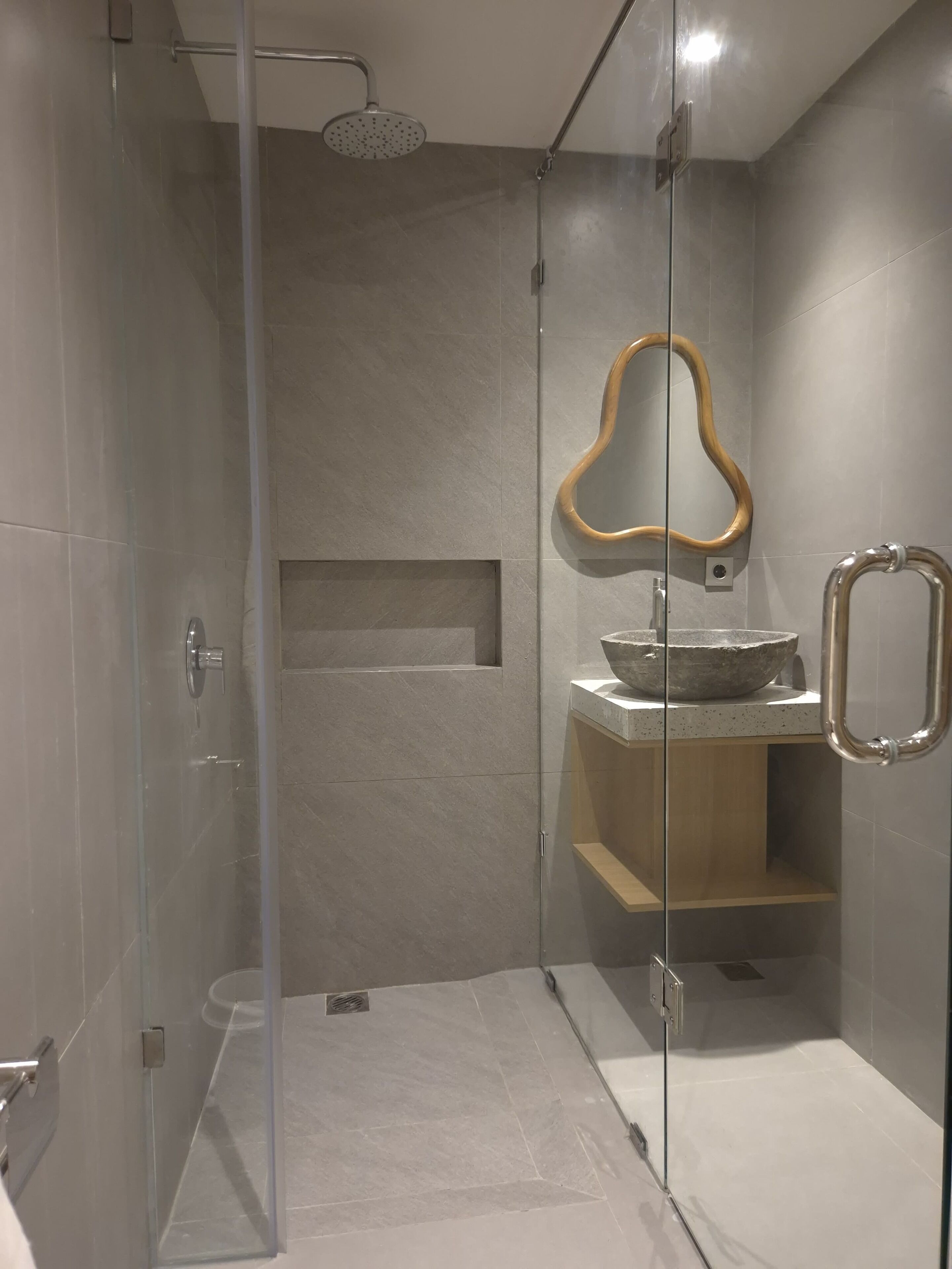 A modern bathroom with a glass-enclosed shower, a wooden-framed mirror, and a stone basin.