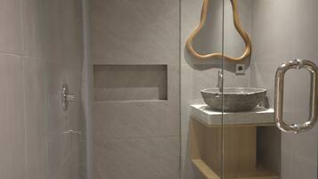 A modern bathroom with a glass-enclosed shower, a wooden-framed mirror, and a stone basin.