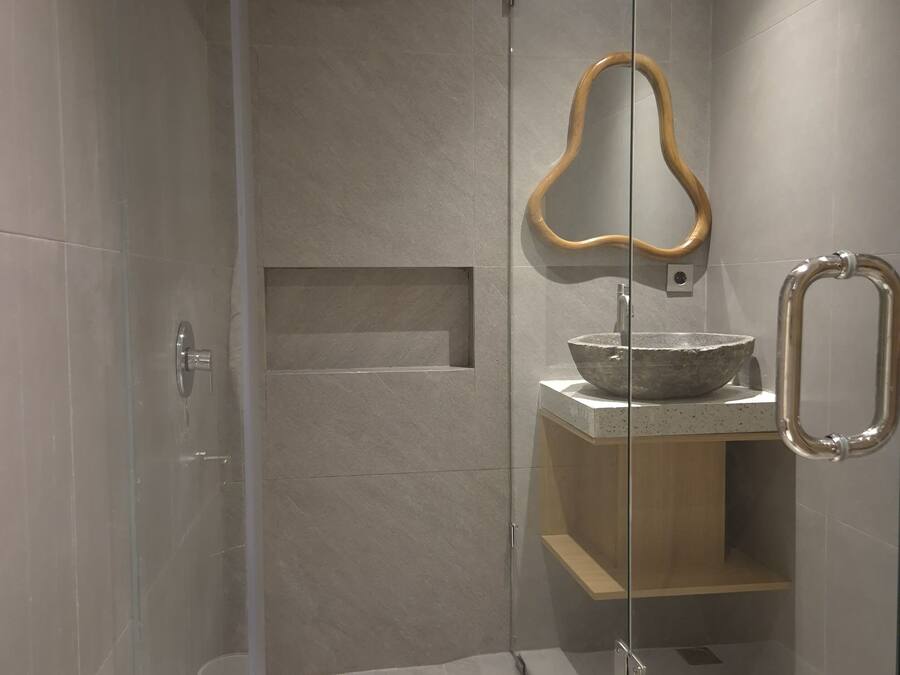 A modern bathroom with a glass-enclosed shower, a wooden-framed mirror, and a stone basin.