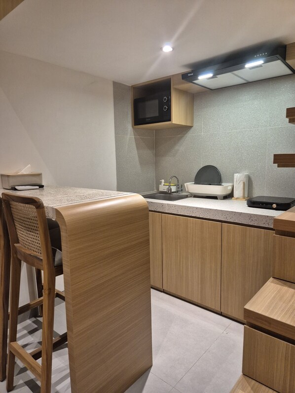 A modern kitchen with a microwave, sink, and bar stools. - Keenan Living Luxe Seturan (Depok)