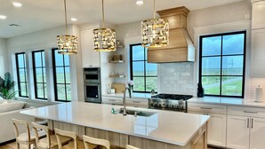 A modern kitchen with a large island, stainless steel appliances, and large windows offering a view of the outdoors. - Luxury Oceanfront Oasis, Private Pool, Steps to Beach (Port Aransas)