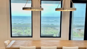 A dining area with a wooden table and four chairs, large windows with a view of the ocean and greenery. - Luxury Oceanfront Oasis, Private Pool, Steps to Beach  (Port Aransas)