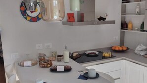 Moderni keittiö, jossa on valkoiset kaapit, keskellä sijaitseva saareke ruokailutiloineen, riippuvalaisimet ja koristeellinen seinäkello.