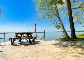 Une table de pique-nique, un drapeau américain, une terrasse en béton et une vue sur le lac.