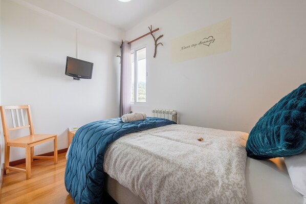 A bedroom with a bed, a chair, a TV, a window, and a motivational quote on the wall. - Casa Os Manos (Santana)