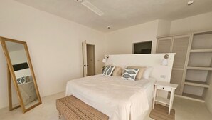 Un dormitorio con una cama grande, una mesita de noche, un banco, un armario y un espejo.
