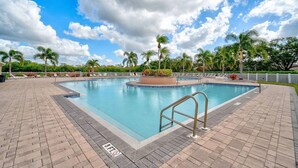 A rectangular swimming pool with a metal ladder, surrounded by a brick deck and palm trees. - Charming 2-bedroom townhome with water view and resort style pool (Bradenton)
