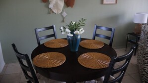 A dining table with four chairs, a vase with white flowers, and woven placemats. - Charming 2-bedroom townhome with water view and resort style pool (Bradenton)