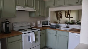 A kitchen with green cabinets, a white stove, a microwave, and a dishwasher. - Charming 2-bedroom townhome with water view and resort style pool (Bradenton)