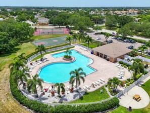 Una piscina con un deck circundante, palmeras y una cancha de tenis al fondo.