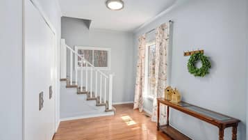 A hallway with a wooden floor, a white staircase, a window with a view, and a small table with a wreath.
