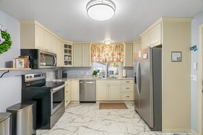 A kitchen with white cabinets, stainless steel appliances, and a marble floor. - Year-Round Hot Tub & Fire Pit - Family Retreat (Coeur d'Alene)