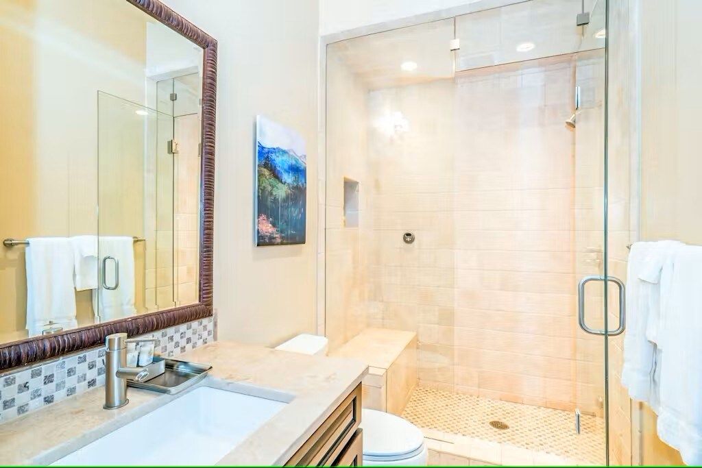 A modern bathroom with a glass-enclosed shower, a sink with a mirror, and a toilet.