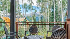 A balcony with wicker furniture, a metal table, and a view of tall trees and mountains. - Trails Edge #1 Ski In/Ski Out (Mountain Village)