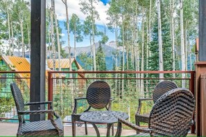 A balcony with wicker furniture, a metal table, and a view of tall trees and mountains. - Trails Edge #1 Ski In/Ski Out (Mountain Village)
