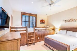 Une chambre à coucher avec un lit, des lits superposés en bois, une télévision, une fenêtre et un ventilateur de plafond.