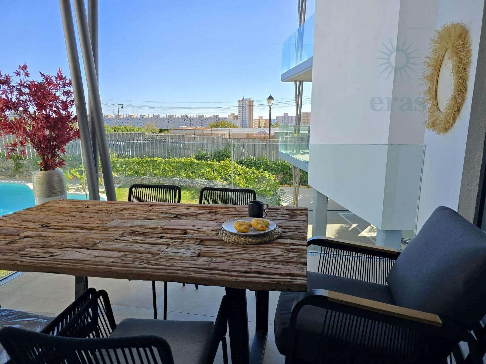 A modern outdoor dining area with a wooden table, black chairs, and a view of the cityscape.