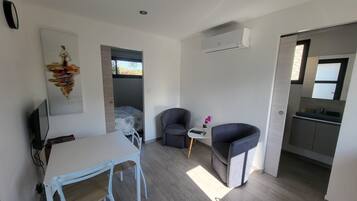 A compact living space with a dining area, two armchairs, a small table with a remote control, and a kitchenette.