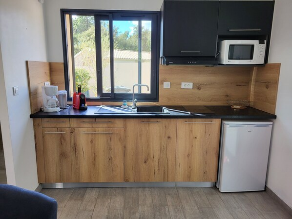 A compact kitchen with wooden cabinets, a microwave, a coffee maker, and a dishwasher.