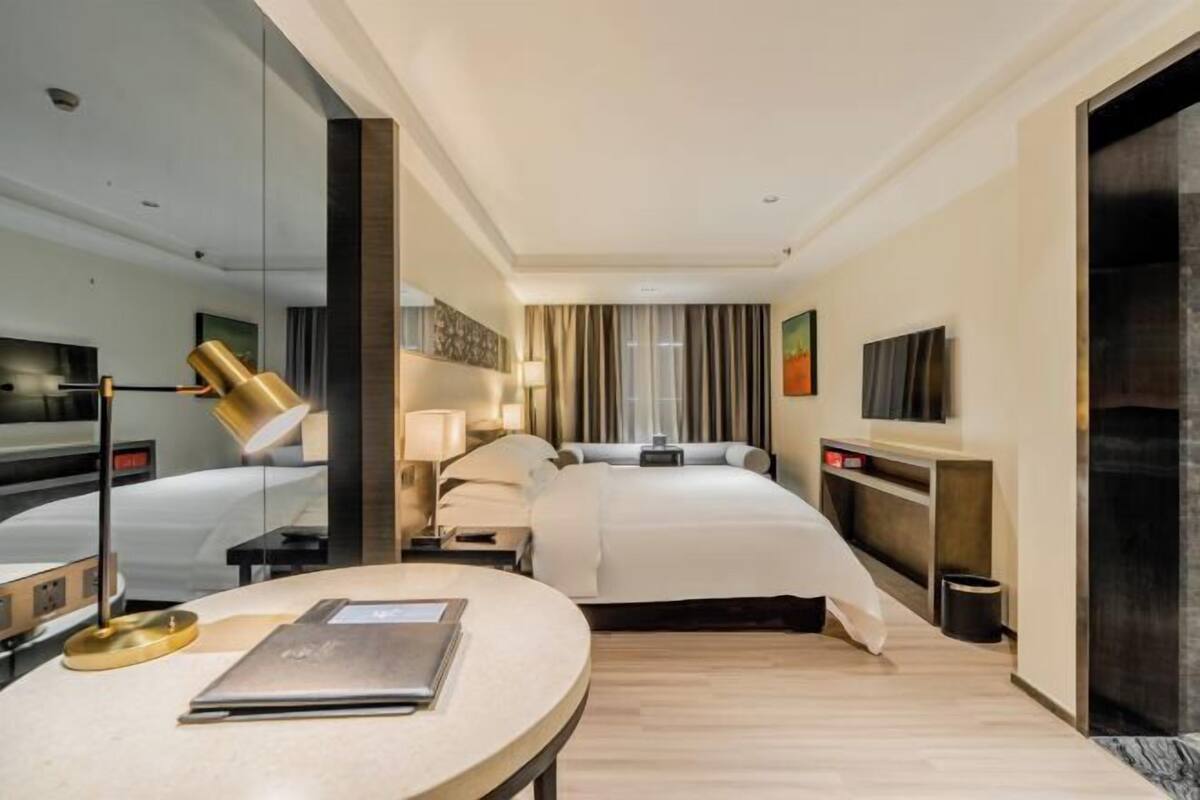 Habitación de hotel con cama, mesitas de noche, escritorio con lámpara, televisor y espejo.