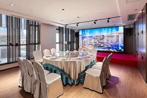 A conference room with a round table, white chairs, and a large screen displaying a cityscape. - La Quay Hotel (Dongguan Houjie Convention and Exhibition Center) (Dongguan)
