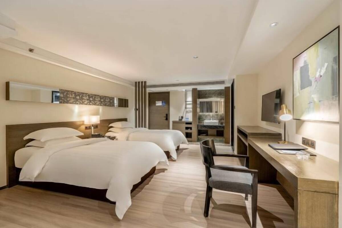 Habitación de hotel con tres camas, un escritorio y una televisión.