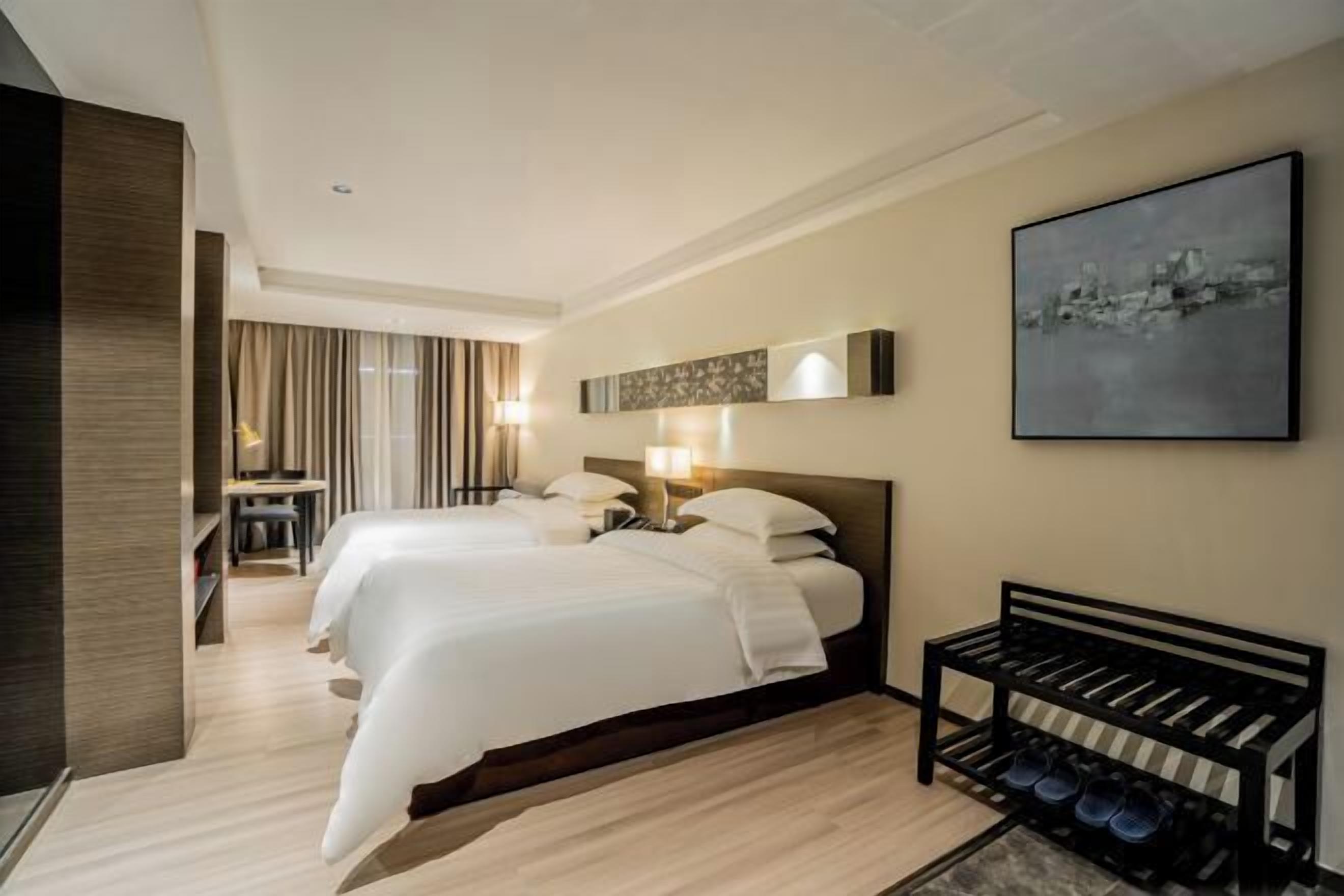 A hotel room with two beds, a shoe rack, a desk, and a chair.