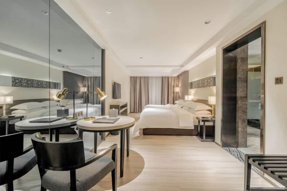 Una habitación de hotel moderna con una cama grande, una mesa redonda de comedor y una zona de estar con sillas.