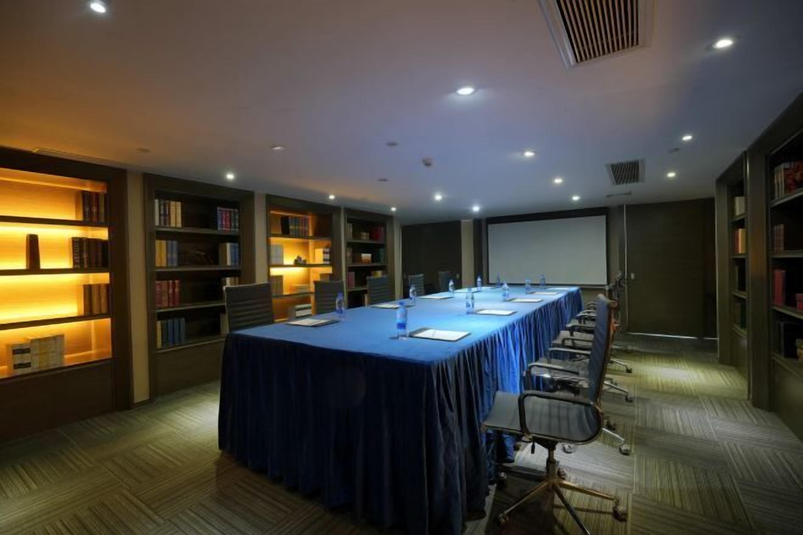 Una sala de conferencias con una larga mesa, sillas y una pantalla para proyector.