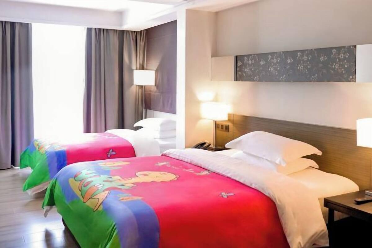 Habitación de hotel con dos camas, una mesita de noche, una lámpara, un cuadro en la pared y una ventana con cortinas.